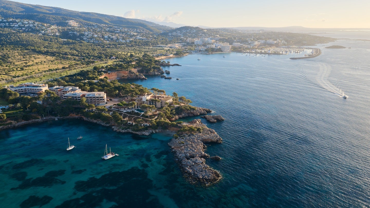 Aerial view of a luxury coastal resort with multiple buildings, lush greenery, and swimming pools overlooking the sea